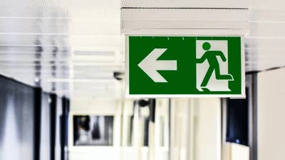 A picture of a green exit sign with an arrow pointing left and a pictogram of a person running through a door